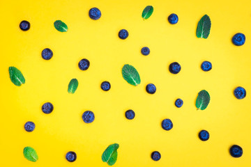 Fresh ripe blueberry with mint leaves on yellow background. Blueberry pattern