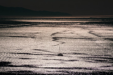 A sailboat floating in the golden from the sun color mediterranean sea in Mykonos, Cyclades, Greece