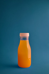 Orange juice bottle on blue background, vertical