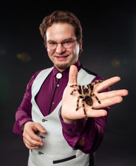 Cheerful man holds thumb up smiling. Magician shows spider tarantula magic show program. Arachnophobia fear concept. Getting rid of a phobia. Huge ugly bird eating. Arachnid home pet