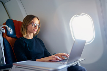Traveling and technology. Flying at first class. Pretty young businees woman working on laptop...