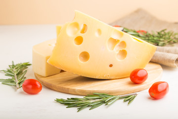 Various types of cheese with rosemary and tomatoes on wooden board on a white wooden background. Side view, close up.