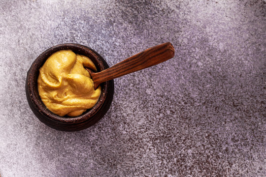 Mustard sauce in bowl with wooden spoon on stone background .Top view, copy space for text