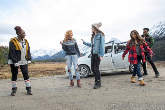 Playful Friends Outside Car At Roadside With Mountain View