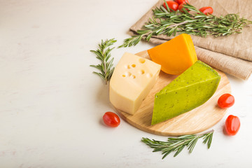Green basil cheese and various types of cheese with rosemary and tomatoes on wooden board on a white wooden background. Side view, copy space.