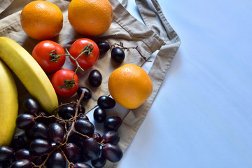 Fresh natural fruits, on an apron, light blue background. Oranges, tomatoes, bananas and black grapes. Natural lighting, space to write.