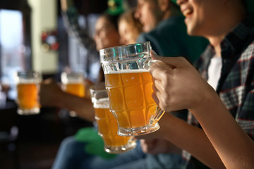 Young friends with beer celebrating St. Patrick's Day in pub, closeup