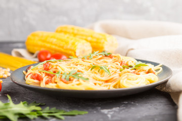 Corn noodles with tomato sauce and arugula on a black concrete background. Side view, selective focus.