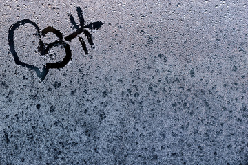 Close-up of love heart with arrow on a wet frozen window.
