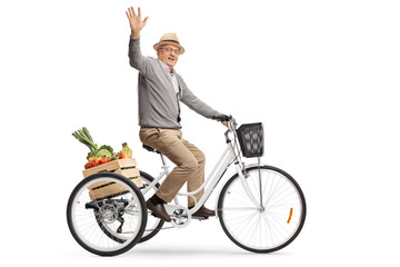 Elderly man riding a tricycle with a crate full of fruits and vegetables and waving at the camera