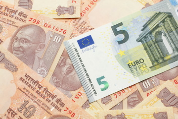 A close up image of a five Euro bank note from Europe in macro with a bed of Indian ten rupee bank notes