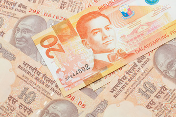 An orange twenty piso bank note from the Philippines with Indian ten rupee bank notes close up in macro