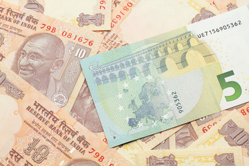 A close up image of a five Euro bank note from Europe in macro with a bed of Indian ten rupee bank notes