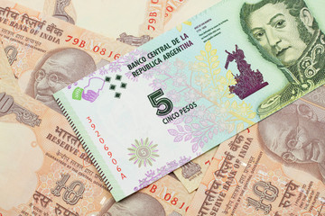 A five peso bank note from Argentina on a background of Indian ten rupee bank notes close up