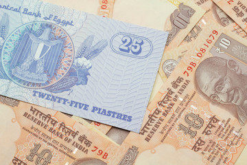 A close up image of an Egyptian twenty five pisatres note with Indian ten rupee bank notes in macro