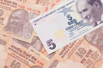 A close up image of a purple five Turkish lira bank note on a background of Indian ten rupee bank notes in macro