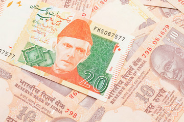 A close up image of an orange and green twenty Pakistani rupee bank note with Indian ten rupee bank notes in macro