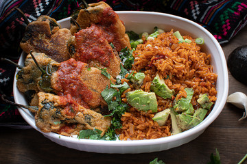 Chiles rellenos and Mexican rice in white dish on wooden table