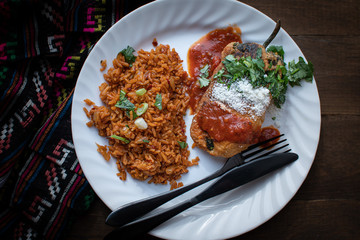 Chiles rellenos and Mexican rice in white dish on wooden table