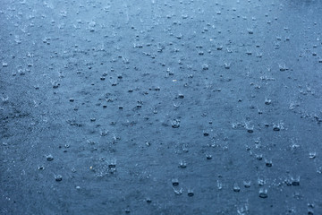 Rain drops rippling in a puddle with blue sky reflection