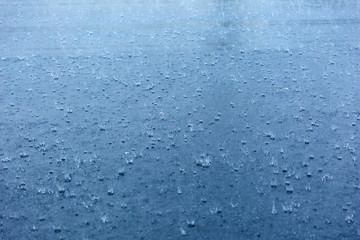 Rain drops rippling in a puddle with blue sky reflection