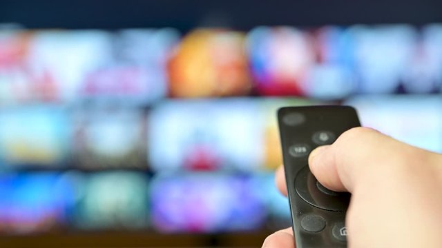 Watch TV. Closeup male hand switches television channels, on the background of the television screen. Interactive tv