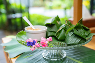 Thailand traditional dessert inside the banana leaf wrap on the glass dish eat with sugar beside it. Arranging on the wood table in the outdoor garden.