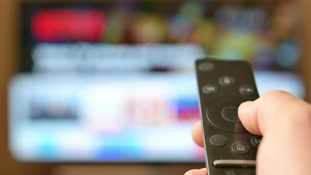 Watch TV. Closeup male hand switches television channels, on the background of the television screen. Interactive tv