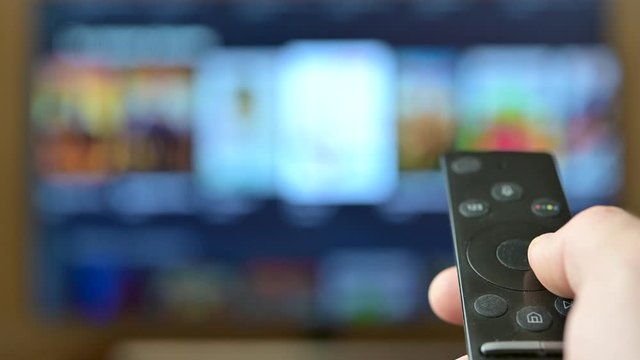 Watch TV. Closeup male hand switches television channels, on the background of the television screen. Interactive tv