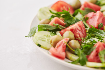 Healthy and tasty salad with tomatoes, green olives, cucumber and rocket on bright stone background. Close up. 