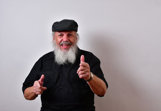 Happy old man is laughing and pointing at the camera..Senior gentleman is laughing and having a great time.. .Mature gentleman with a newsboy cap and black guayabera shirt and long white beard..