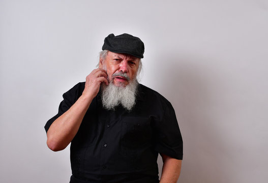 Deep in thought and scratching his beard..Senior is having a thoughtful moment trying to remember.  .. .Mature gentleman with a newsboy cap and black guayabera shirt and long white beard..