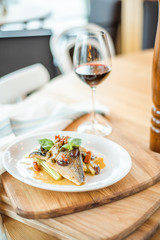 Grilled fish on white plate and wine glasses.