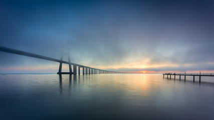 Fototapeta na wymiar Vasco da Gama Bridge and pier over Tagus River in Lisbon, Portugal, at sunrise with a dense fog.