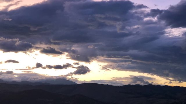 Dramatic red, yellow, and orange clouds at sunset flowing over the Rocky Mountains, time lapse