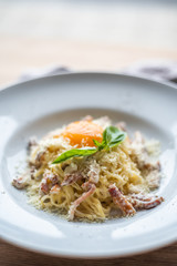 Spaghetti carbonara with pancetta, eggs and cheese in white bowl on the wooden table