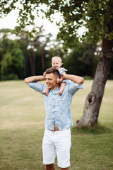 Obraz premium Happy dad and daughter. Dad carries his beloved smiling little girl on his shoulders, outdoors