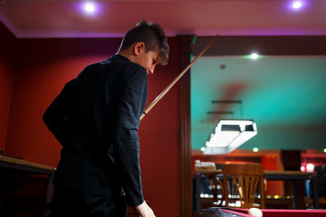 Boy plays billiard or pool in club. Young Kid learns to play snooker. Boy with billiard cue strikes the ball on table. Active Leisure, sport, hobby concept	