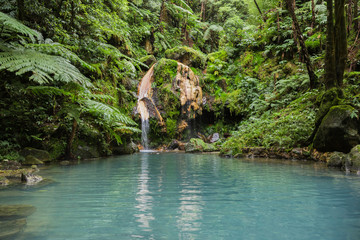Naklejka premium Błękitna laguna naturalnego gorącego źródła w „Caldeira Velha”, gdzie ludzie pływają w ciepłej wodzie na wyspie Sao Miguel, Azory, Portugalia