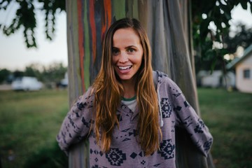A woman hugging a rainbow eucalyptus tree and smiling 