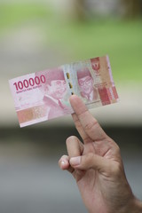 Hold 100,000 Indonesian Rupiahs with fingers. Money for legal payments in Indonesia