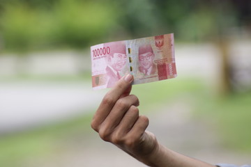 Hold 100,000 Indonesian Rupiahs with fingers. Money for legal payments in Indonesia