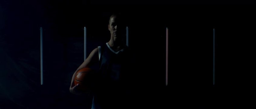 Caucasian female basketball player posing in generic uniform against bright flashing lights, holding ball in her hands. 4K UHD 60 FPS SLOW MOTION shot on ARRI Alexa Mini with Atlas Orion 2x Anamorphic