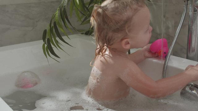 Little two year old girl taking a bath with foam and playing with toys