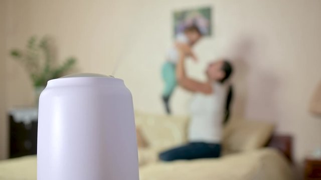 Steam from a working humidifier with ionization of air in the room, against a blurred background, mom plays with the baby on the bed. humidifier works. Climatic device.