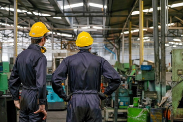 Soft blur image of the back of two technician men stand and look to various type of machine in factory.
