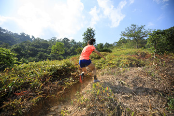 Woman ultramarathon runner running up on mountain slope in tropical forest