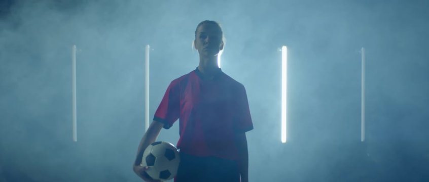 Caucasian female soccer football player posing against bright flashing lights, holding ball in her hands. 4K UHD 60 FPS SLOW MOTION shot on ARRI Alexa Mini with Atlas Orion 2x Anamorphic lens