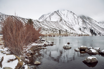 View of Lake on the Mountains in Winter Fog with Dramatic Snow Capped Mountains in the Background 