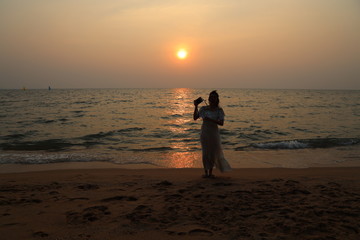 Woman stand beside the sea beach at dawn with the romantic sunset light in summer on her vacation